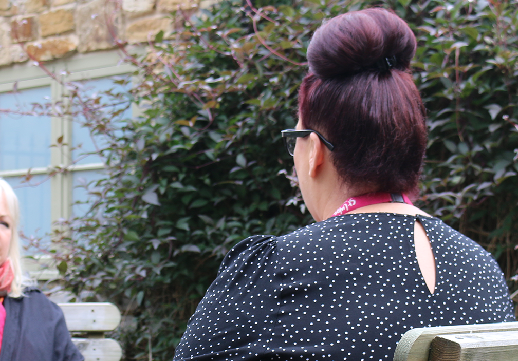 A photograph of Marie Shaw speaking with a client. The client is blurry in the background, just past Marie&#39;s shoulder, and we can see the back of Marie&#39;s head.