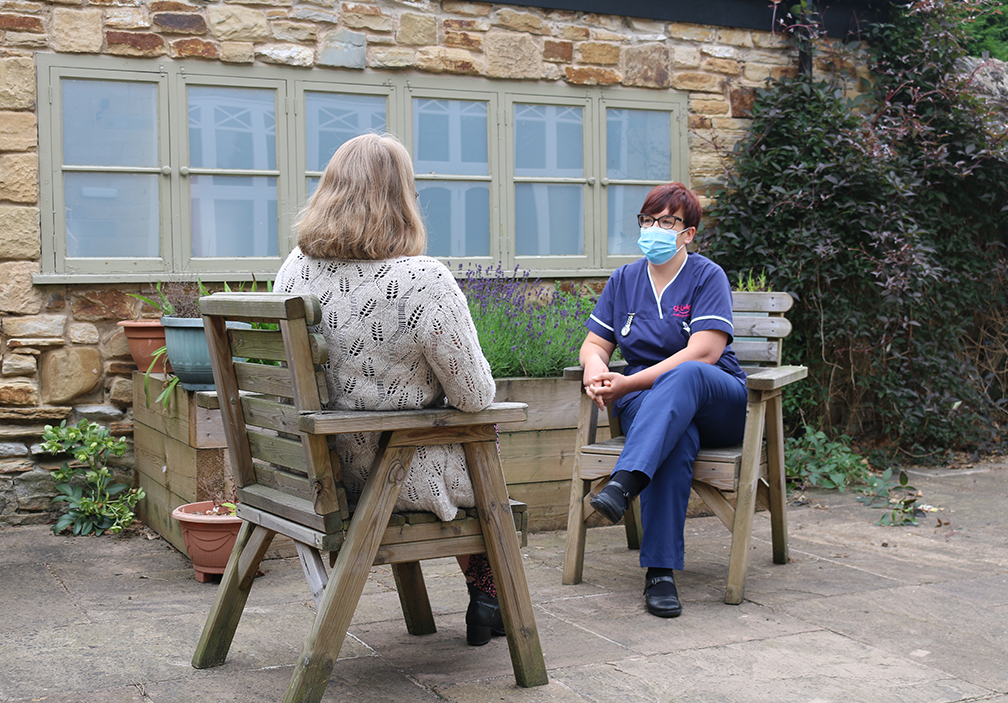 A photograph of Robyn Smith speaking with a patient in the St Luke&#39;s gardens. She is wearing a face mask and listening intently.
